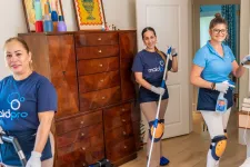 Thumbnail for Three professional house cleaners wearing MaidPro uniforms cleaning a living room and smiling at the camera.