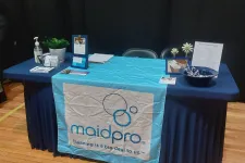 Thumbnail for MaidPro promotional table with cleaning products, brochures, and branded table cover at an indoor event.