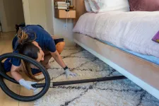 Thumbnail for Person vacuuming a light-colored rug under a bed in a modern bedroom with white gloves.