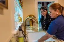Thumbnail for Two women smiling while cleaning a modern kitchen sink with gold faucet and marble countertop