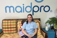 Thumbnail for Smiling woman wearing MaidPro shirt sitting on floral couch with child and MaidPro logo on wall behind.
