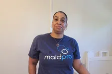 Thumbnail for Woman in a navy blue MaidPro t-shirt stands indoors next to a white cleaning supply container.