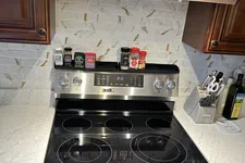 Thumbnail for Modern stainless steel electric stove with spice jars on backsplash and wooden kitchen cabinets
