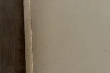 Thumbnail for Corner of a beige wall meeting a wooden floor with a white baseboard and tile flooring above it.
