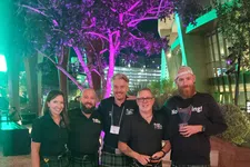 Thumbnail for Group of five people wearing green plaid kilts and black tops posing outdoors at night with colorful tree lighting.