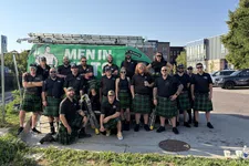 Thumbnail for Group of men and women wearing matching black shirts and green kilts posing outdoors by a green work van.