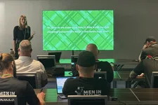 Thumbnail for Presenter giving a presentation to seated attendees with a green slide about Men In Kilts company future vision.