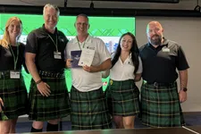 Thumbnail for Group of five people wearing green plaid kilts, smiling and holding certificates in front of a green screen.