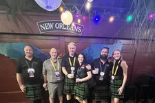 Thumbnail for Group of six people wearing kilts at a New Orleans venue with hanging lanterns and colorful string lights