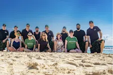 Thumbnail for Group of people in kilts and casual wear posing on sunny beach with blue sky and ocean in background