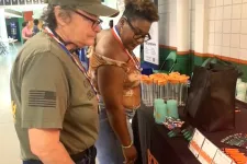 Thumbnail for Two women examining promotional items on a table at an indoor community event or expo.