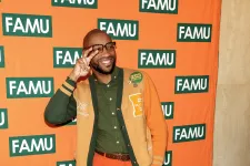 Thumbnail for Man in orange and green outfit posing joyfully with FAMU backdrop at an indoor event