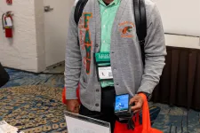 Thumbnail for a man wearing a backpack and lanyard standing next to a table with a bottle of water