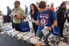 Thumbnail for Attendees browse informational materials at a conference booth in a busy event space with patterned carpet.