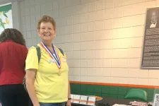 Thumbnail for Woman in yellow shirt standing next to a German Shepherd service dog at an education event booth.