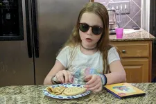 Thumbnail for Child wearing sunglasses enjoys snacks at a kitchen counter surrounded by fridge magnets and a colorful book.