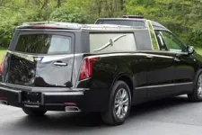 Thumbnail for Black hearse parked on a scenic road surrounded by greenery and trees.