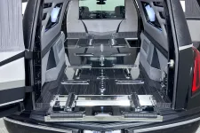Thumbnail for Interior view of a luxury hearse with open rear doors showing polished metal floor and chrome fixtures.