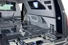 Thumbnail for Interior view of a modern, polished hearse with sleek, reflective coffin mounts and soft gray upholstery.