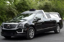 Thumbnail for A black Cadillac hearse parked amidst greenery, showcasing its sleek design and spacious rear.
