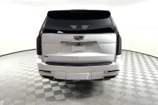 Thumbnail for Rear view of a white Cadillac SUV in a well-lit showroom with checkered flooring and tinted windows.