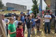 Thumbnail for Group of people of various ages gathered outdoors near a construction site on sunny day