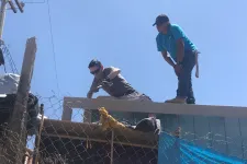 Thumbnail for Two construction workers on a rooftop under clear blue sky working on building framework.