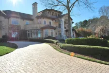 Thumbnail for Luxury mansion with stone driveway, manicured bushes, tall columns, large windows under clear blue sky.