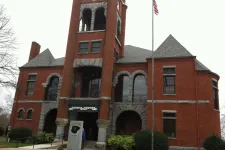 Thumbnail for Historic red brick courthouse with clock tower and American flagpole in front on cloudy day