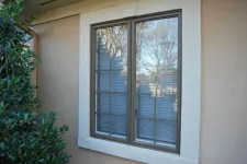 Thumbnail for Reflective double-pane window with blinds on beige stucco wall next to green shrubbery outside a residential home.