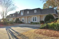 Thumbnail for Single-story beige house with dormer windows, surrounded by bushes and trees in a sunny suburban setting.