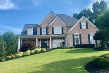 Thumbnail for Large brick two-story house with black shutters, manicured green lawn, and trees under a blue sky.