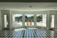 Thumbnail for Bright room with black and white patterned floor, large windows, and a balcony with chairs and plants