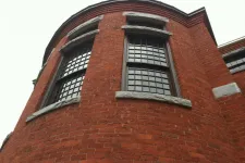 Thumbnail for Curved red brick building facade with large multi-pane windows and stone accents under an overcast sky