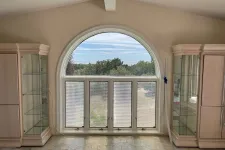 Thumbnail for Bright room with large arched window, beige cabinets, glowing tiled floor, and outdoor greenery view.