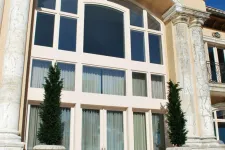 Thumbnail for Grand entrance with tall arched windows, marble columns, and potted evergreen trees under clear blue sky.