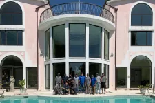 Thumbnail for Group of people posing by a large modern house with tall windows and a swimming pool in front.