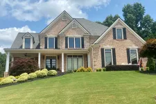Thumbnail for Spacious two-story brick house with black shutters and well-maintained front yard under a blue sky with clouds