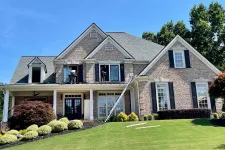 Thumbnail for Brick two-story house with black shutters undergoing window installation on a sunny day with green lawn.