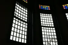 Thumbnail for Tall windows with grid patterns and colorful stained glass panels at the top in a dark interior setting