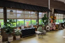 Thumbnail for Indoor garden shop display with potted plants, woven baskets, floral arrangements, and a black storage cabinet under wooden windows.