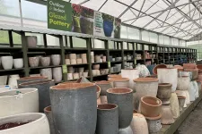 Thumbnail for Rows of glazed pottery pots in various sizes displayed on shelves inside a greenhouse garden center.