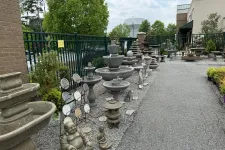 Thumbnail for Outdoor garden center display featuring stone fountains, statues, and decorative ornaments on gravel and pavement.