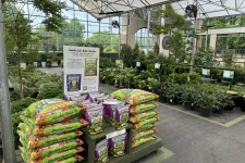 Thumbnail for Bags of Dr. Earth soil and fertilizer displayed in a greenhouse with plants and trees in the background.