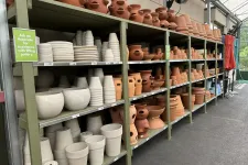 Thumbnail for Shelves filled with various terra cotta and ceramic flower pots in a greenhouse nursery aisle.
