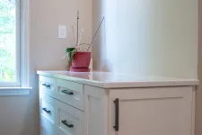 Thumbnail for White kitchen cabinetry with black handles beside a window and a small plant on the countertop under recessed lighting.