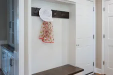 Thumbnail for White entryway bench with dark wood top, coat hooks holding a hat and scarf, next to white doors and wood floors.