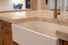 Thumbnail for Modern kitchen with a white farmhouse sink, brass faucet, wooden cabinets, and beige marble countertop.