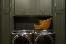 Thumbnail for Modern laundry room with dark green cabinets, front-load washer and dryer, and wicker baskets on countertop.