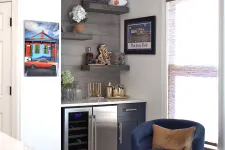 Thumbnail for Cozy corner with blue swivel chair, built-in wine fridge, floating shelves, and framed wall art near a window with blinds.